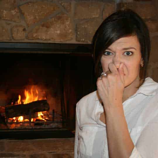 Person plugging nose near fireplace because a chimney draft problem is a common cause for stinky odors in your home