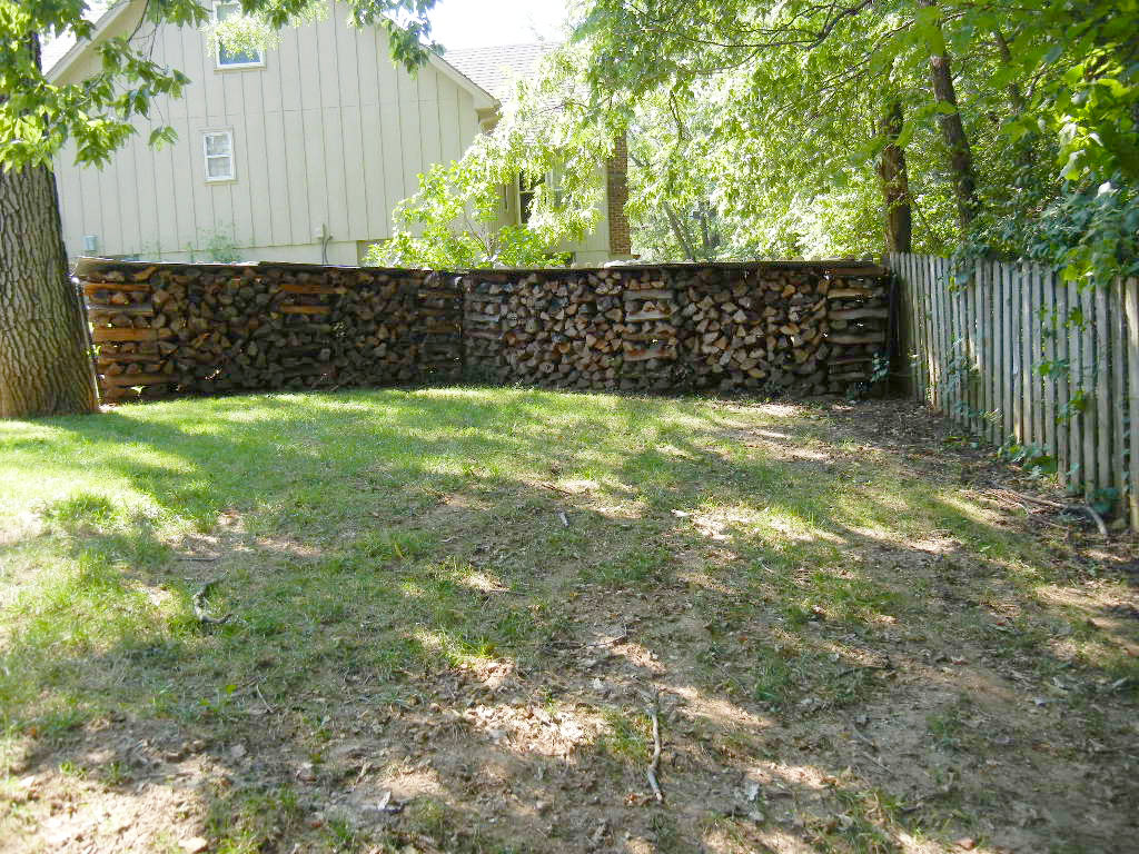 covered and cross stacked wood along a fence in backyard