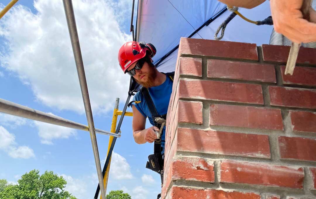 Chimney Technician tuckpointing brick masonry chimney during a complete restoration