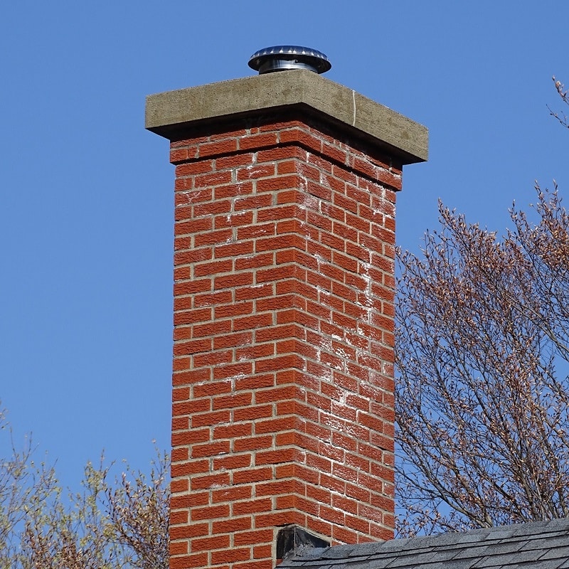 Red brick chimney against blue sky with treetops