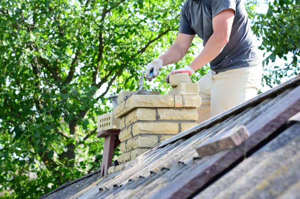 Bricklayer repair brick chimney on house rooftop