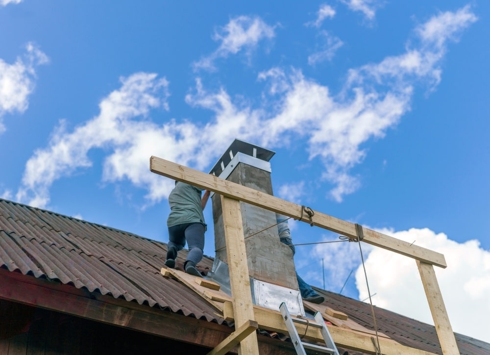 two workers standing on rooftop and repairing chimney