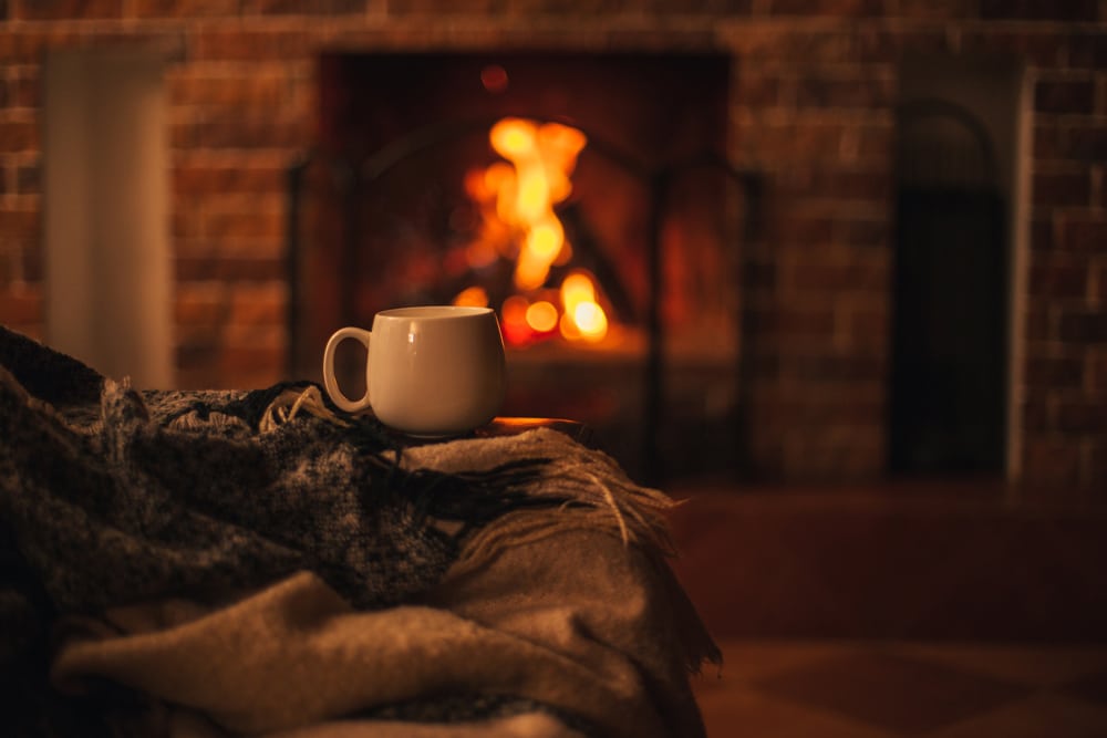 Cozy white mug of steaming hot tea beside a warm fireplace in a comfortable living room, highlighting safe winter relaxation for Kansas City homes.